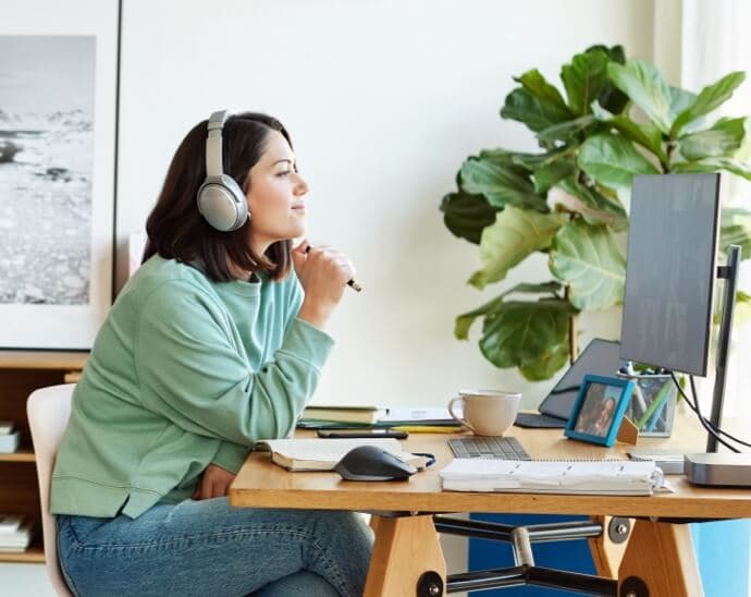 Mulher usando fones de ouvido, segurando uma caneta e olhando para um monitor de computador