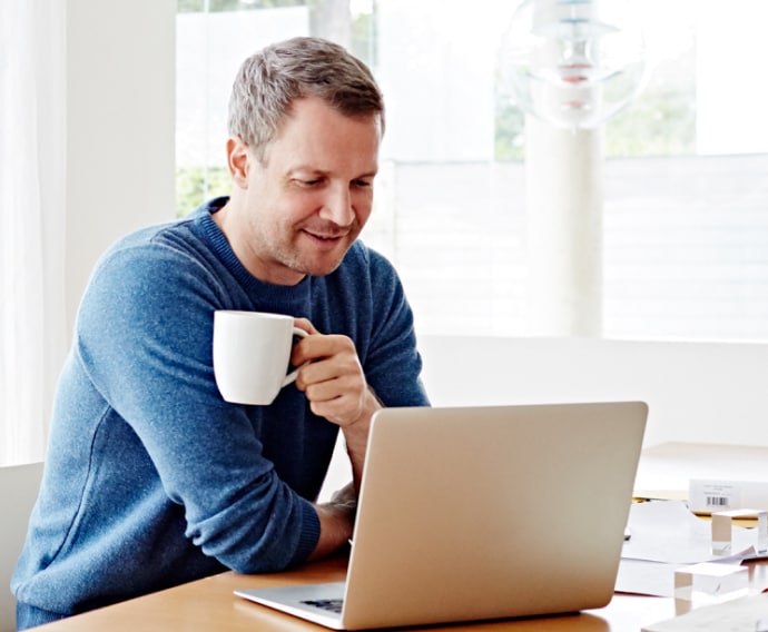 Homem em casa usando laptop e tomando café.