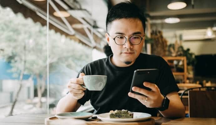 Homem tomando café olhando para o telefone celular, com o Norton 360 Standard sendo inicializado.