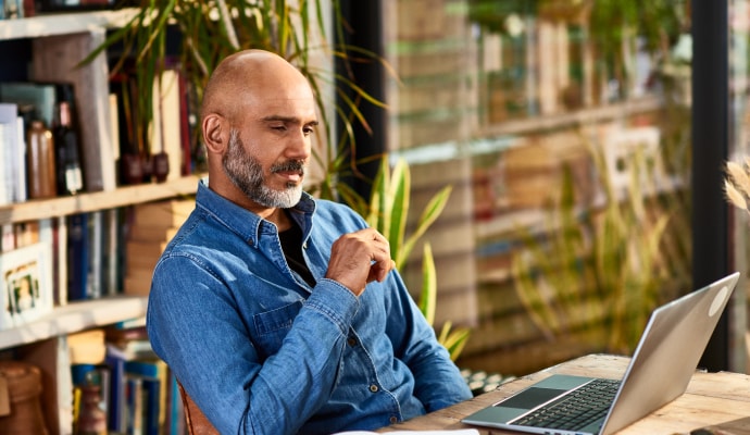 Homem sentado a uma mesa olhando para um notebook